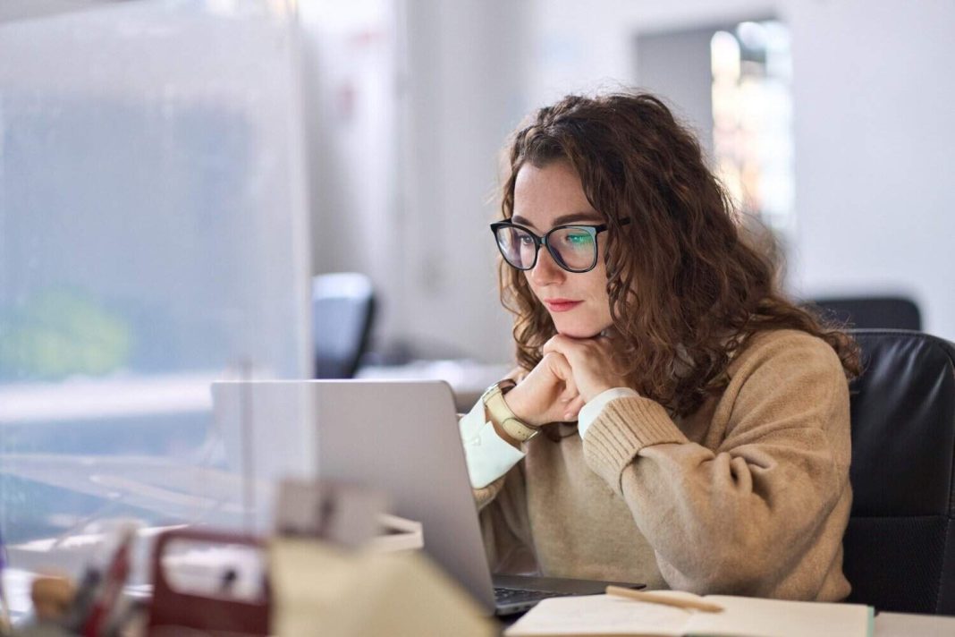 A young woman sits in front of a laptop looking at tips about how to us AI to search for a home with Redfin. 