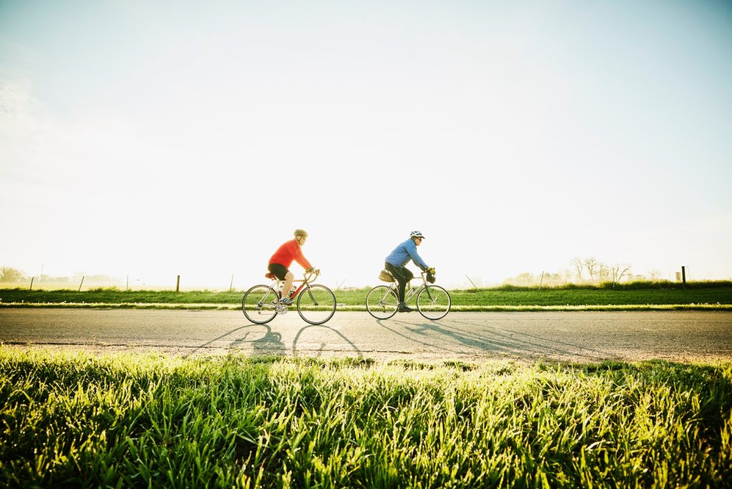Wide shot of senior male friends on sunrise bike ride on rural road